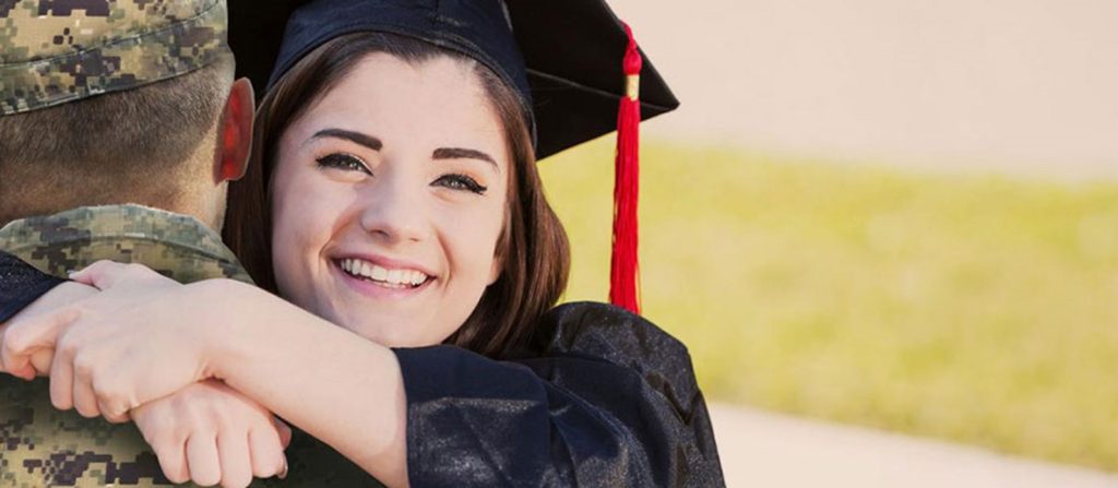Teenage girl wearing graduation gown hugging loved one in military uniform