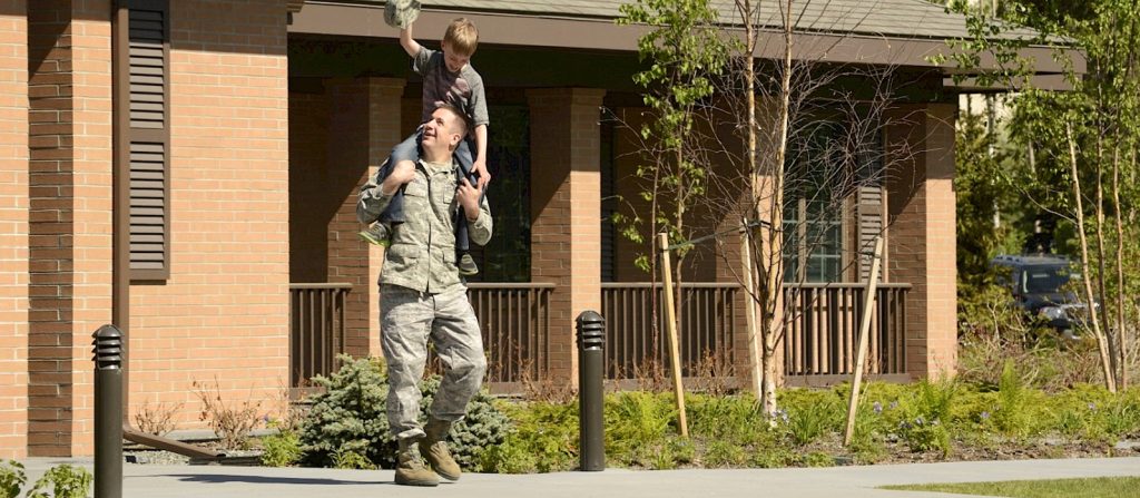 Solider smiling as they carry a kid on their shoulders